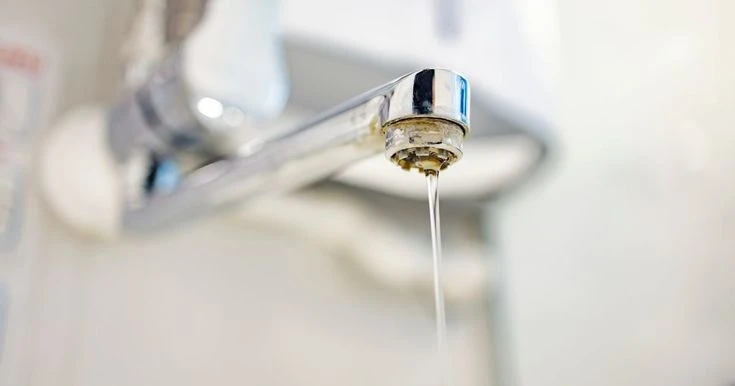 Dépôts de calcaire blanc sur une canalisation et un robinet de salle de bain entartré